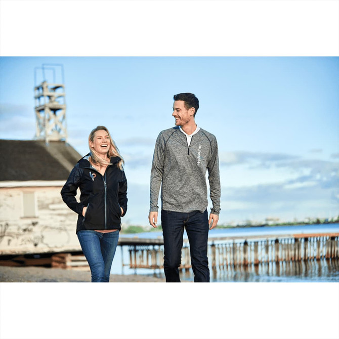A woman wearing a black softshell jacket walks beside a man in a grey long-sleeve top by the water.