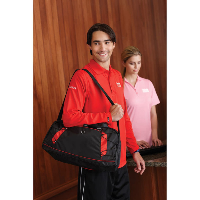 A man in a red polo shirt with black accents carries a bag, while a woman in a pink polo shirt stands nearby.