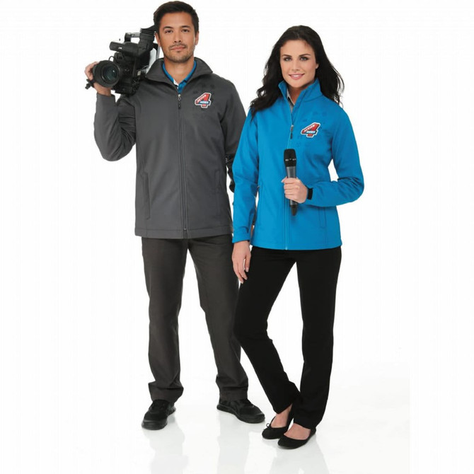 A softshell jacket for women in blue, featuring a logo, displayed by a model holding a microphone.