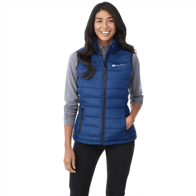 A woman wearing a blue insulated vest with a zip front and side pockets, styled with a grey long-sleeve top.