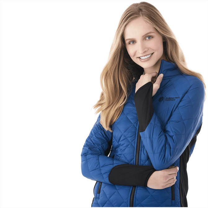 A woman in a blue insulated jacket with black sleeves, featuring a logo on the chest.