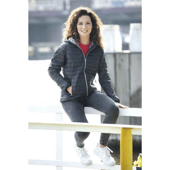 A woman is sitting on a railing wearing a black packable insulated jacket, paired with grey jeans and white sneakers.