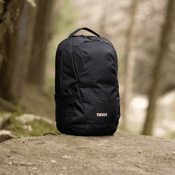A black laptop backpack with a side pocket and a logo, set against a natural outdoor background.