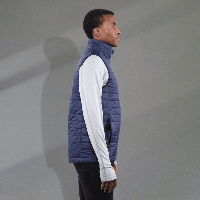 A navy puffer vest with a high collar, worn over a long-sleeve white top, featuring a logo on the chest.