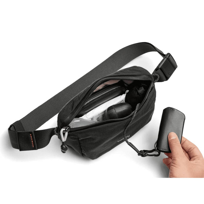 A black Bellroy Lite Belt Bag with an open zipper, revealing various items inside, including a drink bottle and an umbrella.