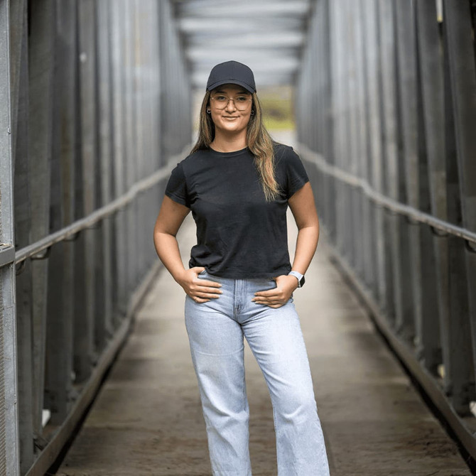 A woman wearing a black Falcon Flex Cap and a black t-shirt, standing confidently on a bridge.