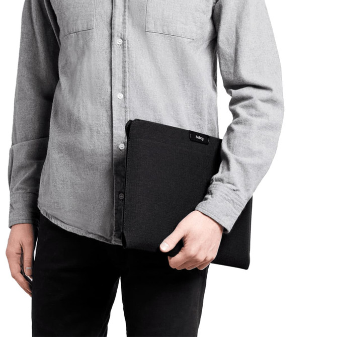 A laptop sleeve in black held by a person wearing a grey shirt, showcasing a sleek and minimalist design.