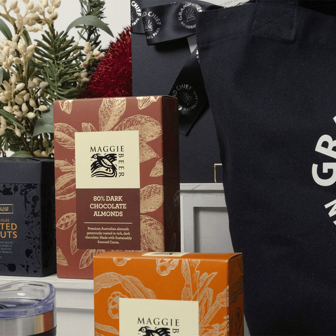 A gift pack featuring dark chocolate almonds, assorted nuts, and a black tote bag with a logo. Includes decorative elements.