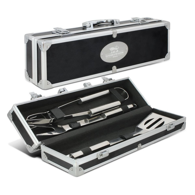 A black and silver BBQ tool set in a metal case, featuring a spatula, tongs, and a fork.