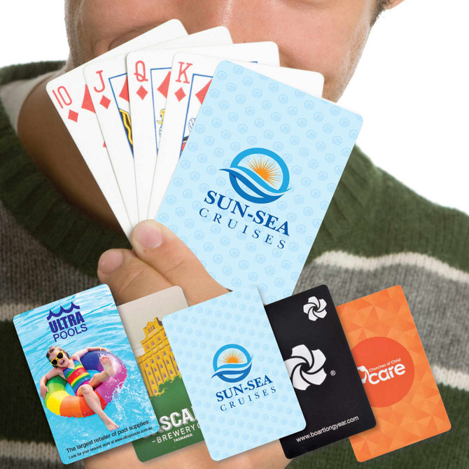 A person holding a fan of playing cards featuring various designs and colors, including logos and promotional cards.