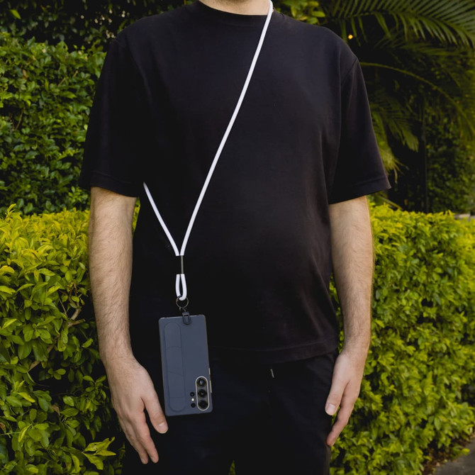 A phone lanyard in white, secured to a smartphone, is draped across a person’s body against a green background.