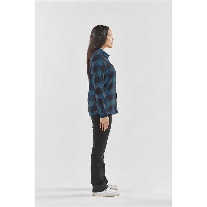 A side view of a woman wearing a blue and black checkered button-up shirt with black jeans and white shoes.