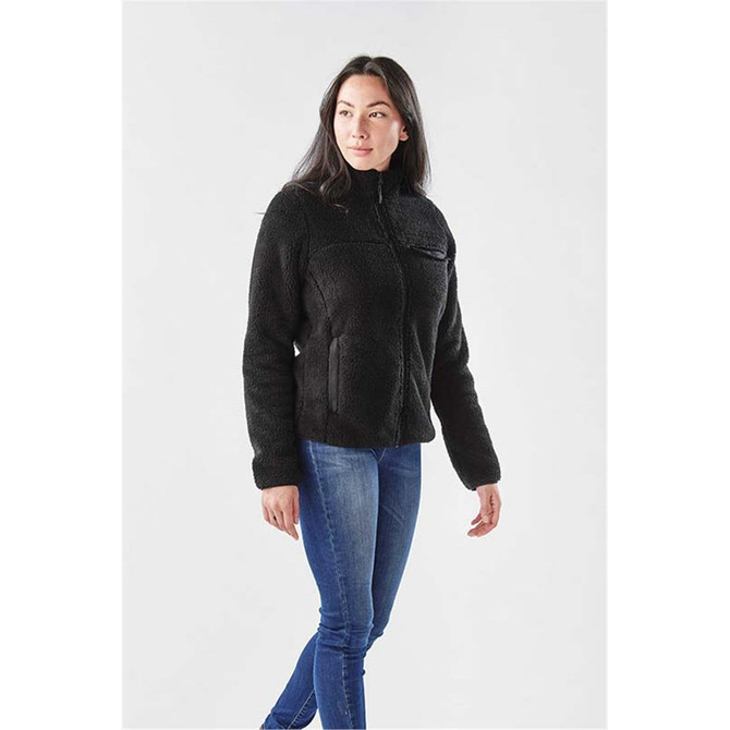 A women's black sherpa fleece jacket with a zip-up front and a pocket, worn over blue jeans.