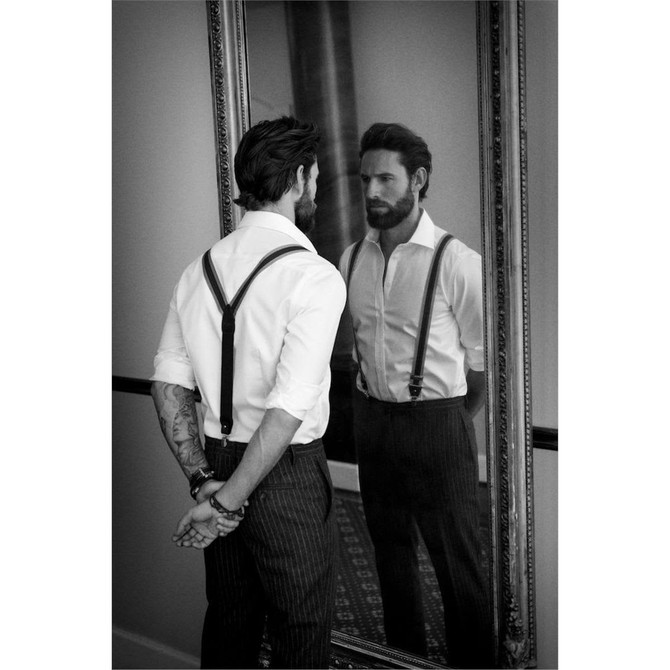 A men's button-up shirt in white, featuring a fitted design and worn with black suspenders, reflected in a mirror.