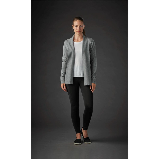 A woman wearing a grey Women's Soho Cardigan over a white top, paired with black leggings. The background is dark.