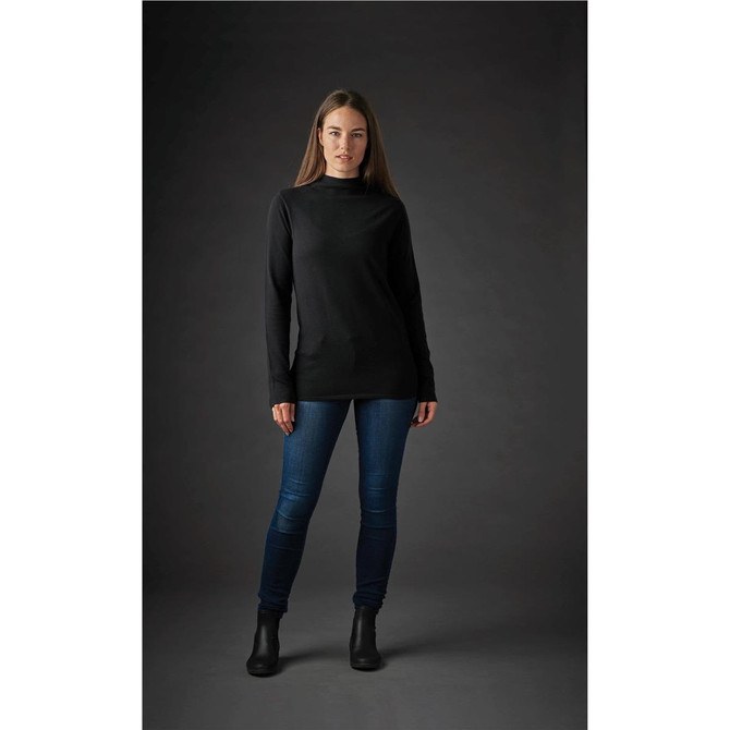 A woman is wearing a black Women's Belfast Sweater with a simple design, paired with blue jeans and ankle boots.