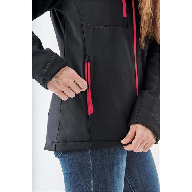 A close-up of a black softshell jacket with pink zippered pockets, being worn by a person.