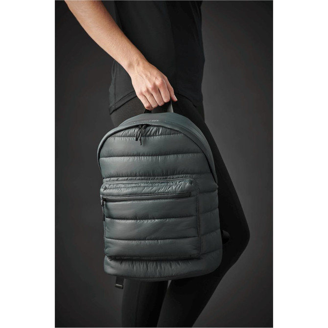 A dark green quilted backpack held by a person, featuring a front pocket and a simple design.