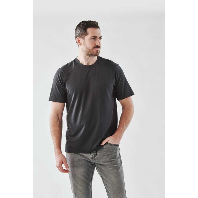 A man wearing a black short sleeve performance T-shirt, styled with casual jeans, against a light grey background.