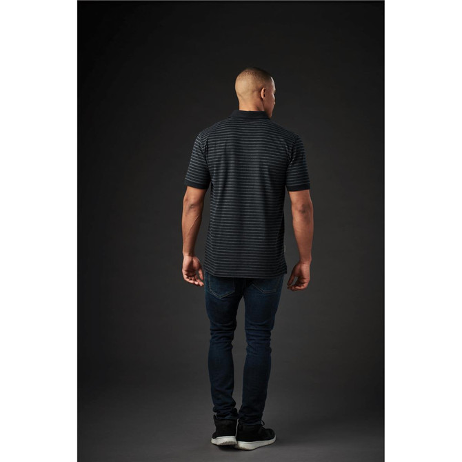 A back view of a man wearing a dark striped polo shirt paired with dark jeans. The shirt features a logo.