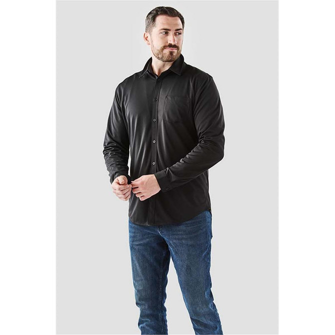 A man wearing a black long sleeve button-up shirt, paired with blue jeans, standing against a neutral background.