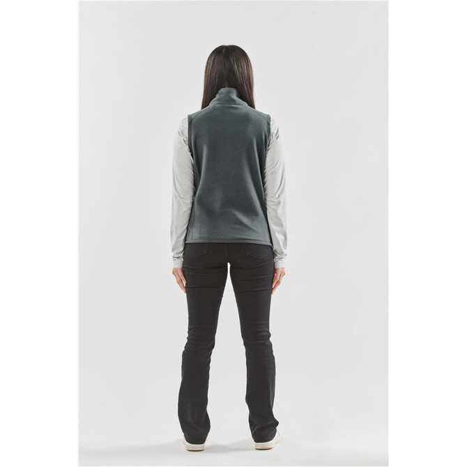 A woman stands with her back to the camera, wearing a grey fleece vest over a long-sleeved shirt, paired with black pants.