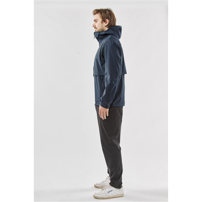 A navy blue technical shell jacket with a hood, featuring a logo, worn by a person standing sideways.
