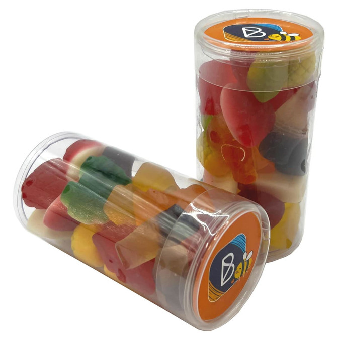 A clear tube filled with mixed lollies in various colours, including red, yellow, green, and orange. The tube features a branding logo.