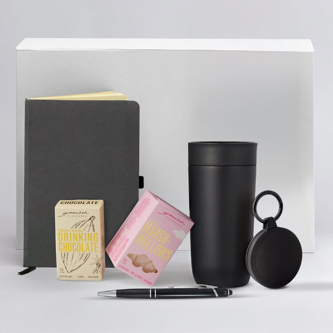 A drink bottle, notebook, pen, and boxes of drinking chocolate and marshmallows in a monochrome setting.