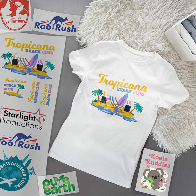 A white t-shirt featuring a colourful design with beach elements and logos, arranged on a flat surface.