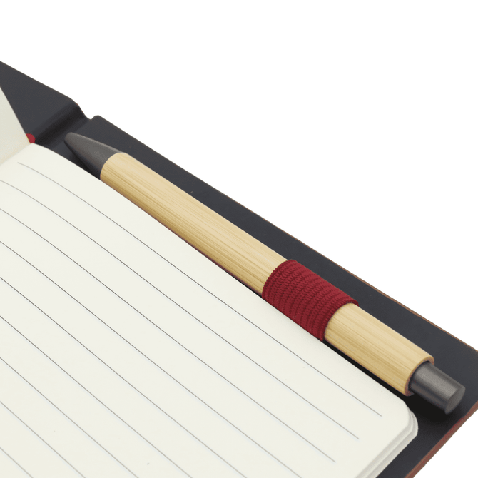 A dark notebook with lined pages and a bamboo pen with a red grip placed inside.