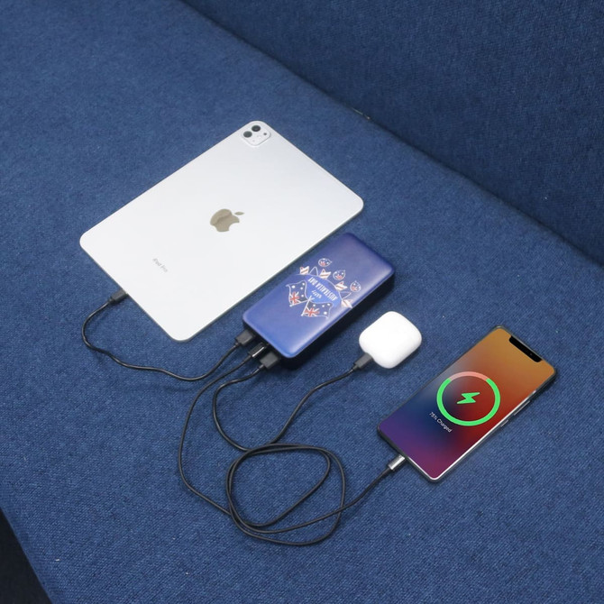 A blue power bank with a logo, connected to a phone and tablet, charging on a blue fabric surface.