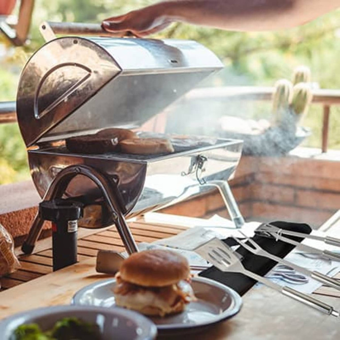 Three-piece barbecue tool set in black pouch, featuring stainless steel utensils, placed on a wooden table near a barbecue.