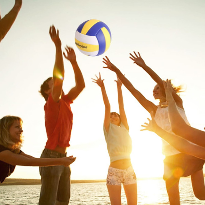 A volleyball with blue and yellow panels is being tossed among several people silhouetted against a sunset.
