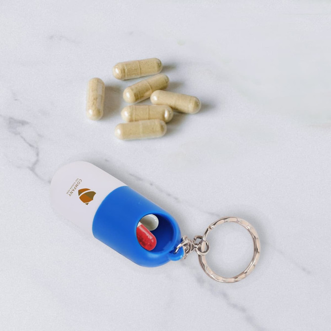A blue and white pill capsule keychain with several beige capsules beside it, featuring a logo.