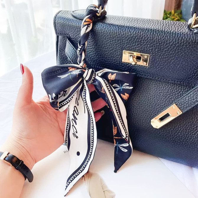 A silk chiffon scarf in navy, featuring a floral pattern, tied elegantly to a black handbag.