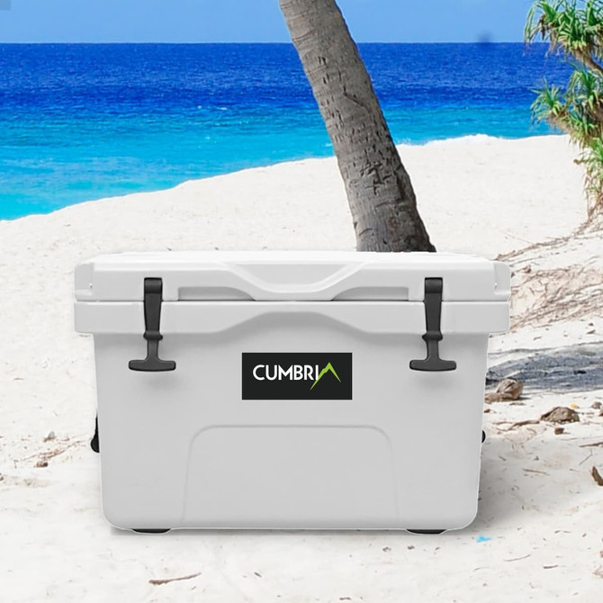 A white 25L cooler box with a logo, set on a sandy beach near palm trees and blue water.