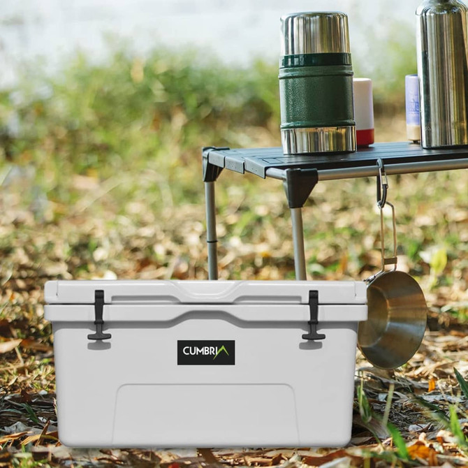 A white 85L cooler box sits on the ground, with drink bottles and utensils nearby. It features a logo.