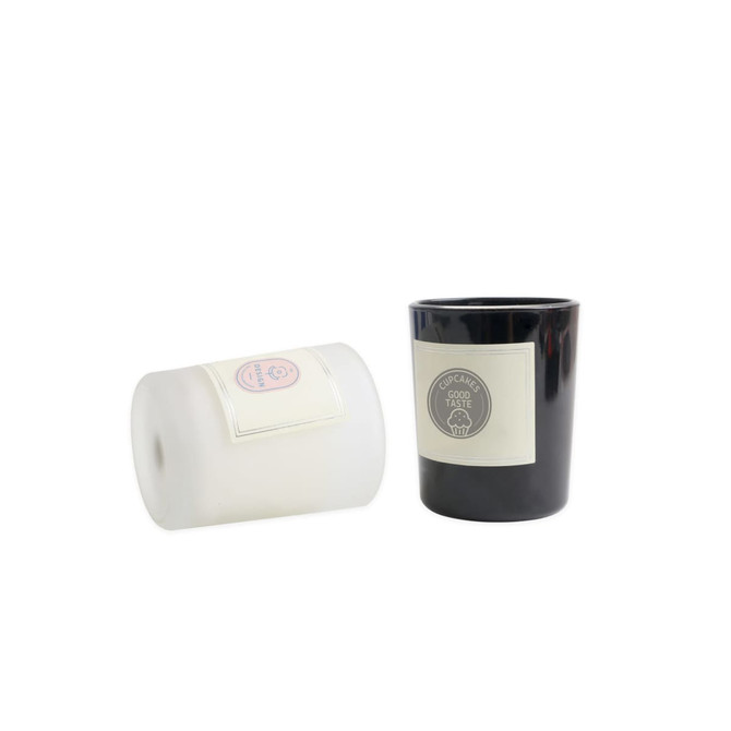 Two glass candles, one white and one black, featuring labels and a logo.