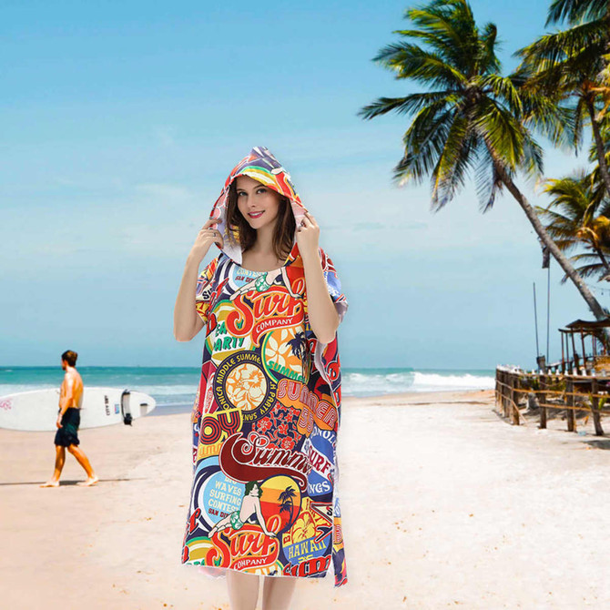 A vibrant, multicoloured hooded towel with a surf theme, featuring various playful graphics, set against a beach backdrop.