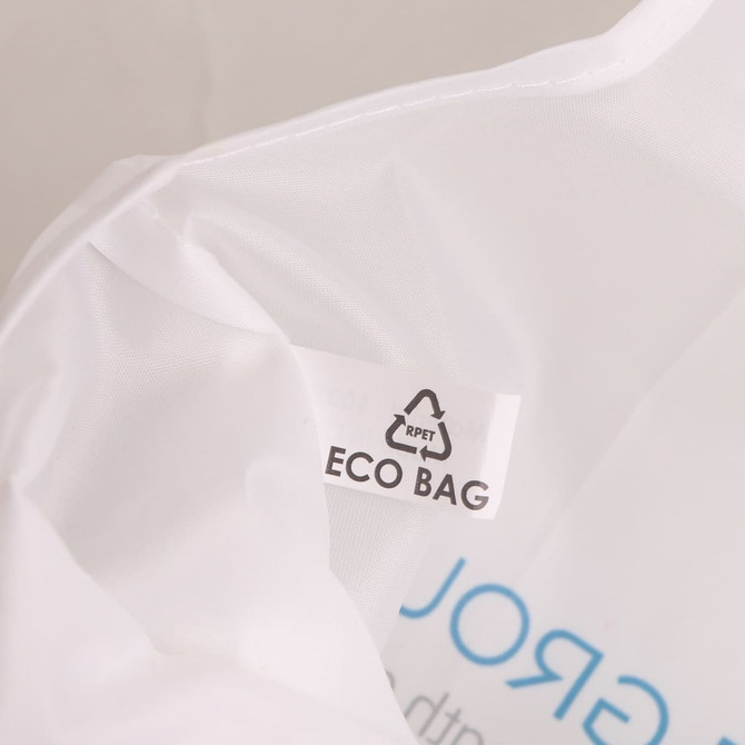 A close-up of a white foldable shopping bag with a logo and eco-friendly label inside.