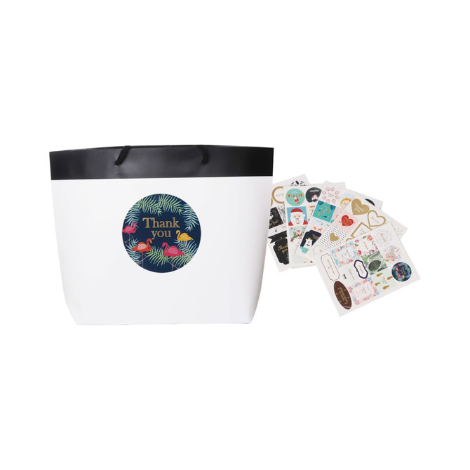 A small black and white boutique paper bag with a black rim and assorted decorative stickers beside it.