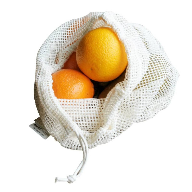A white organic cotton mesh bag containing three oranges, with a drawstring closure and a visible logo.