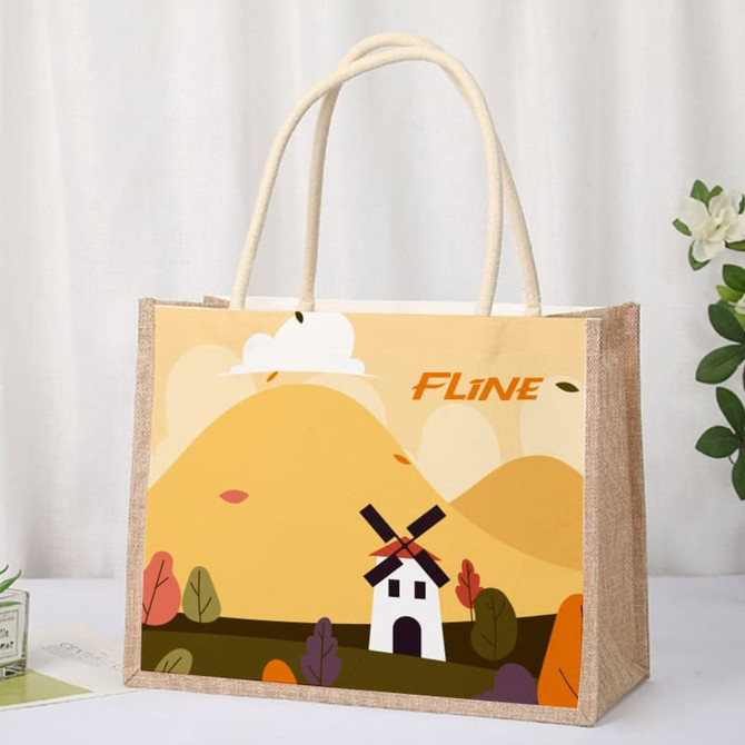 A jute tote bag with a patterned canvas front featuring a windmill and hills in yellow and green tones.