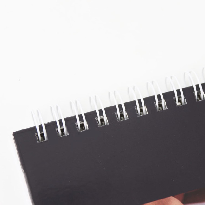 A black desk calendar with a spiral binding at the top, featuring a smooth, matte cover.