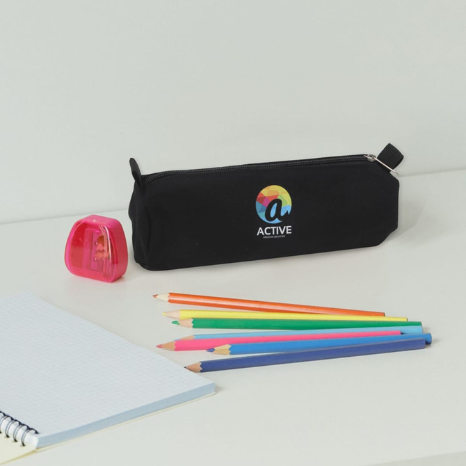 A black canvas pencil case with a logo, surrounded by coloured pencils and a pink sharpener on a desk.