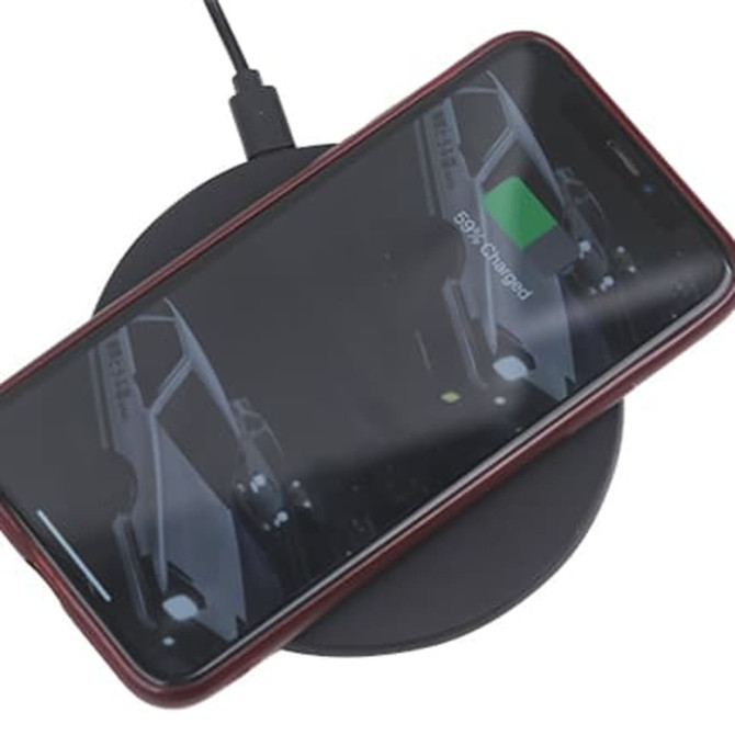 A black wireless charger with a smartphone placed on top, connected to a power source.