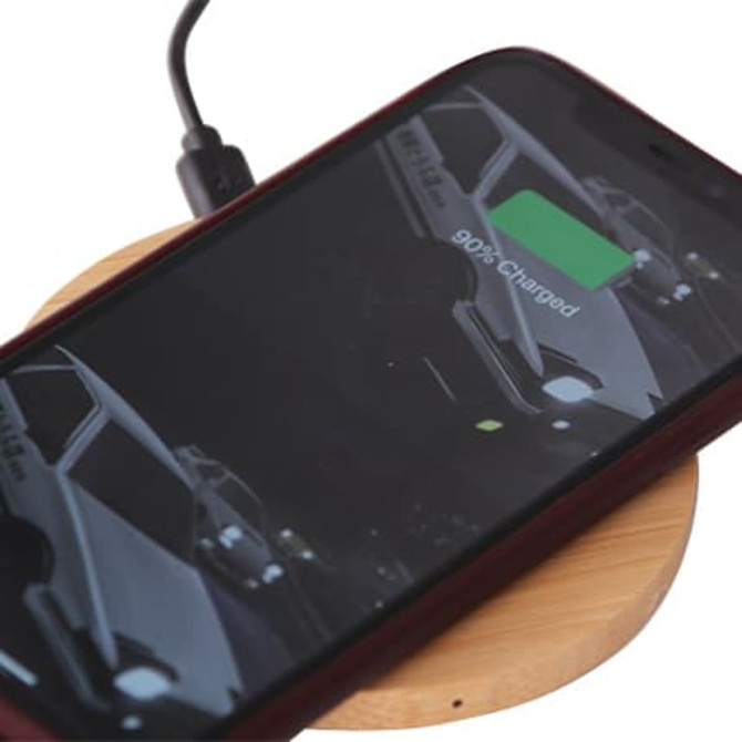 A bamboo wireless charger with a smartphone placed on it, showing a charging indicator.