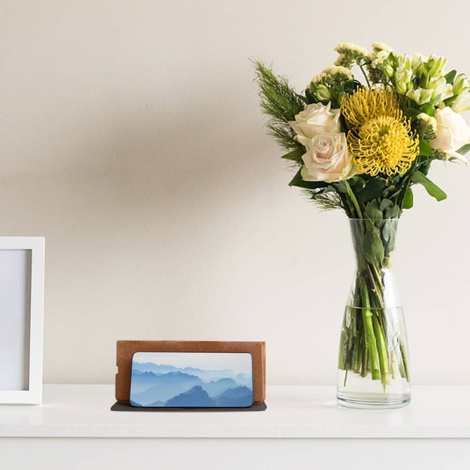 A foldable cork wireless charger in a natural wood finish, placed beside a vase of flowers on a shelf.