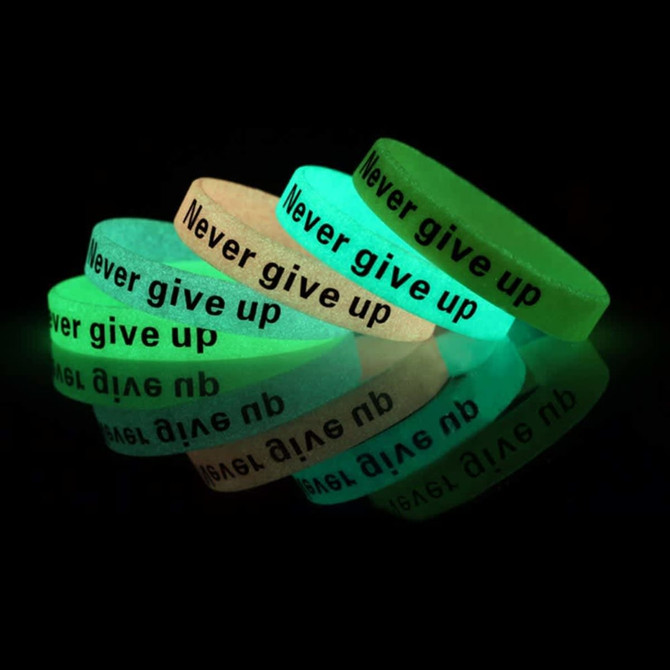 A set of glow-in-the-dark silicon wristbands in green and white with black text. They feature a motivational phrase.